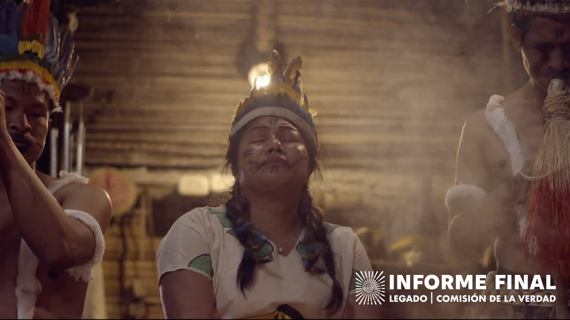 Mujer indígena con la cara pintada mirando hacia arriba con los ojos cerrados, sobre su cabeza una corona de plumas
