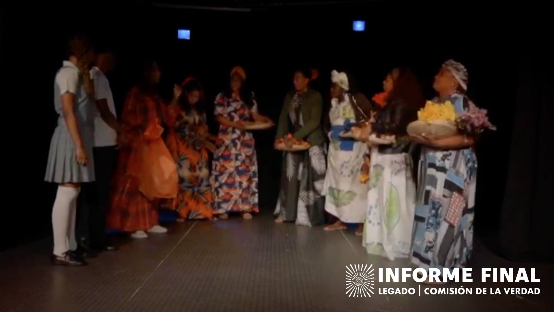 Obra de teatro, medio círculo de mujeres con vestidos tradicionales, algunas con bandejas de flores en las manos