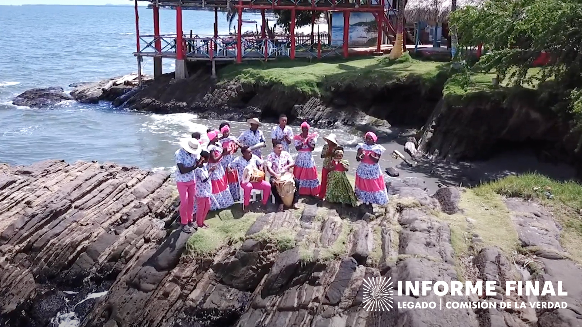  Grupo de personas con tambores y vestidos tradicionales cantando en una piedra a la orilla del mar