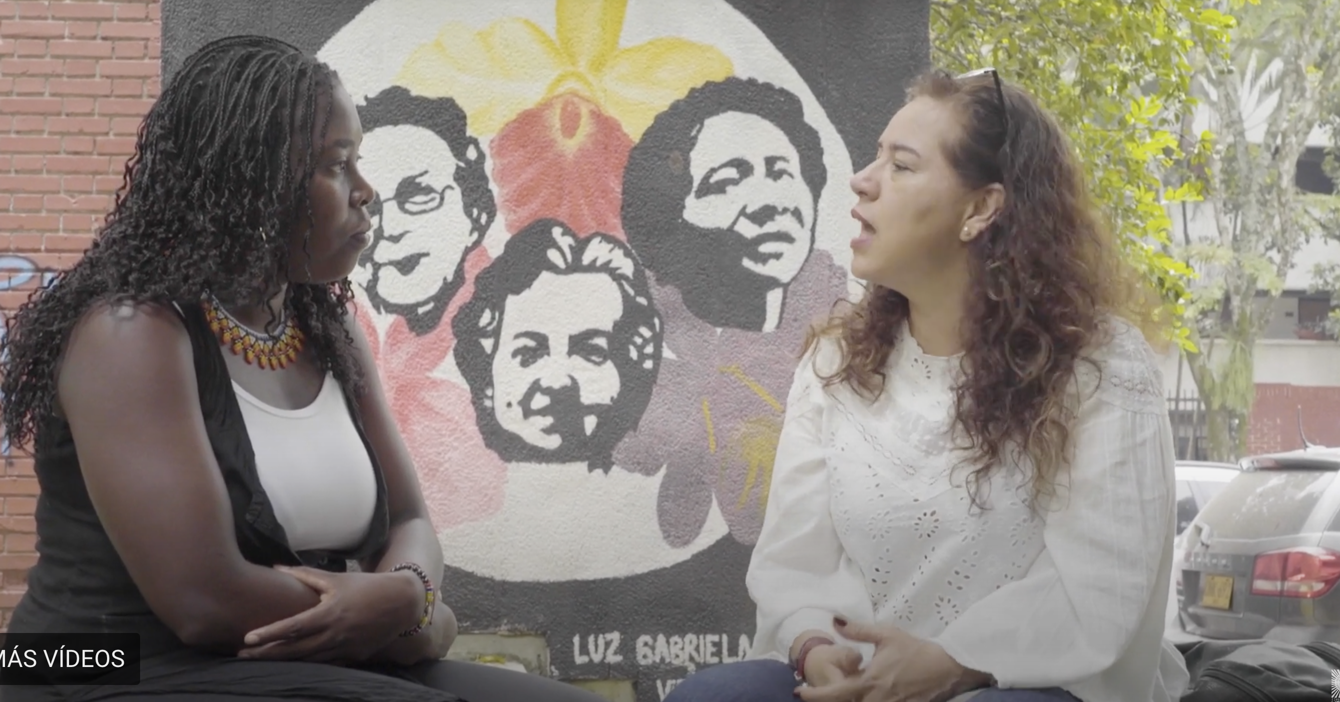 mujeres conversando en un espacio urbano con un mural de fondo