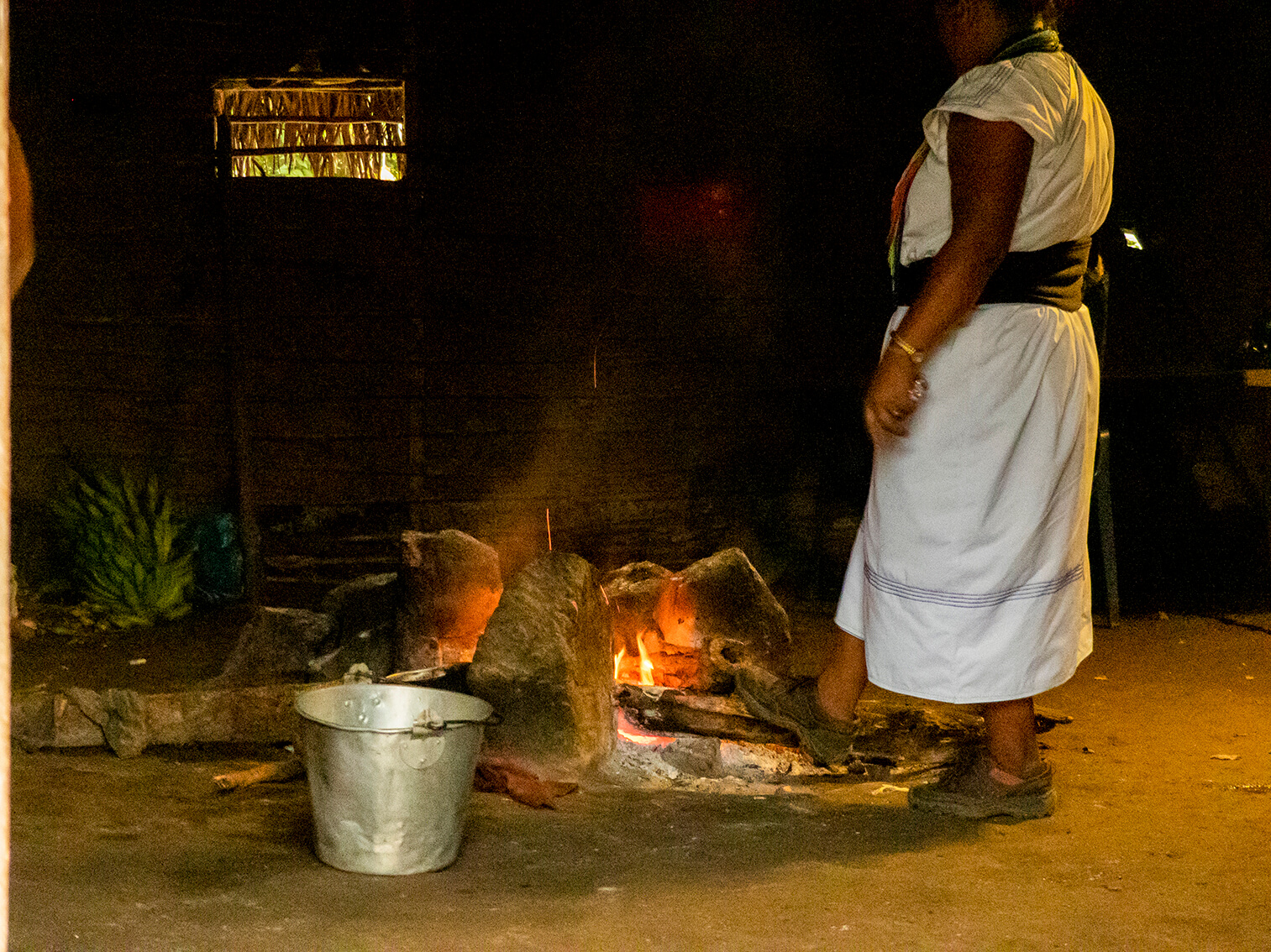Para mantener encendido el fuego en una cocina de leña arhuaca, una mujer empuja un pedazo de madera con su pie derecho.