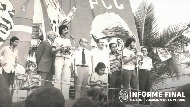 Captura fotográfica antigua, grupo de personas, dos de ellas hablan por micrófono. Al fondo banderas y la siglas "PCC"