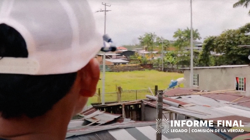 Hombre con gorra blanca de espaldas mirando. En el fondo techos de casas y una zona verde con pequeña tribuna