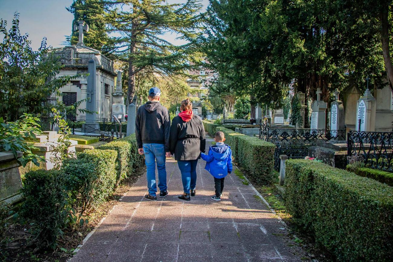 hombre, mujer y niño de espaldas y tomados de la mano caminando por un cementerio