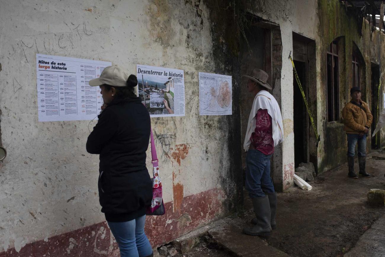 2 Personas observan afiches pegados a los muros en la fachada de una edificación abandonada