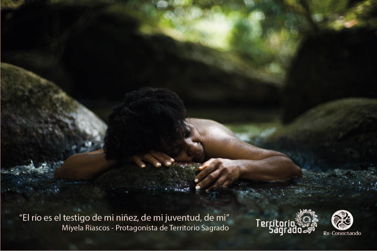 Mujer afro reposa desnuda, boca abajo sobre la piedra de un río. texto de Miyela Riascos: “El río es el testigo de mi niñez, de mi juventud, de mí”