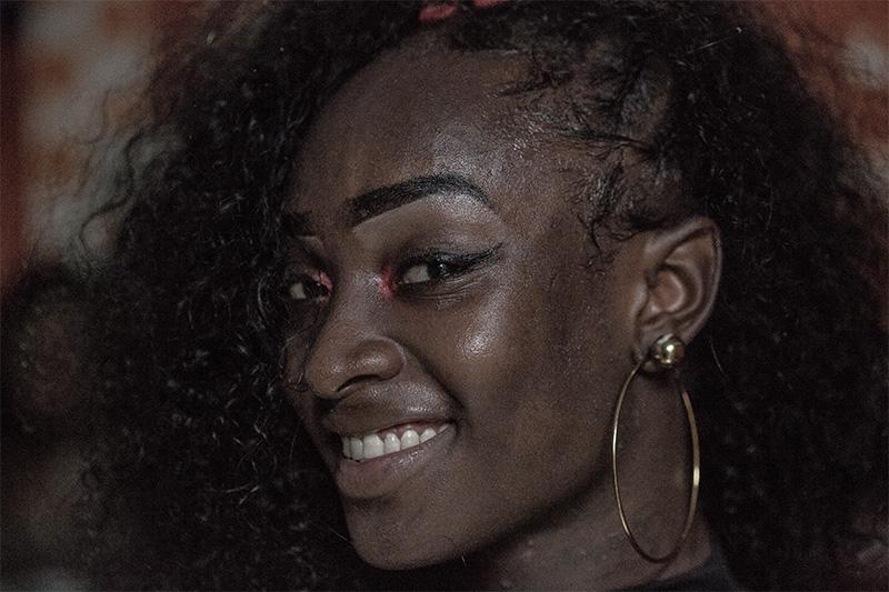 Mujer afro con maquillaje en los ojos, cabello recogido a un lado y candongas sonríe.