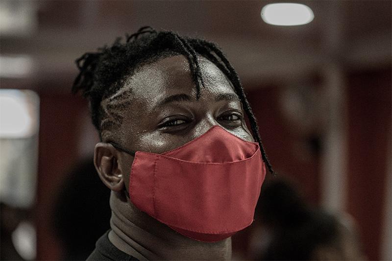 Hombre afro con tapabocas rojo, dos trenzas caen sobre su rostro, sonríe