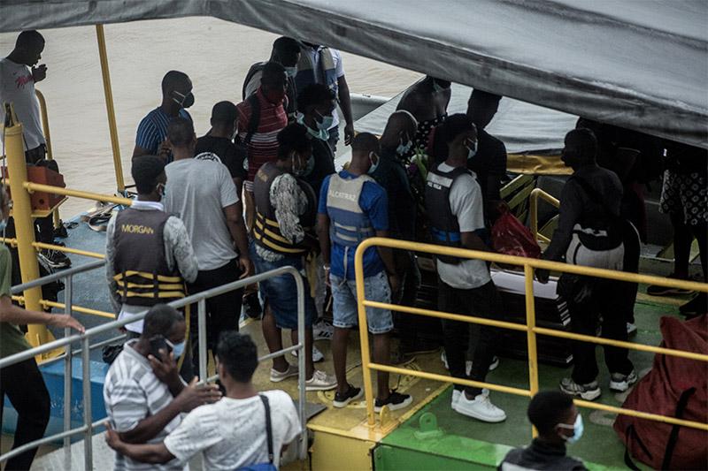 Hombres afro se están subiendo a un ferry, algunos llevan chalecos salvavidas puestos