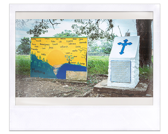 Instantánea. Sepulcro, al lado memorial con pintura sobre muro con sol entre montañas, la palabra “memoria” y nombres escritos