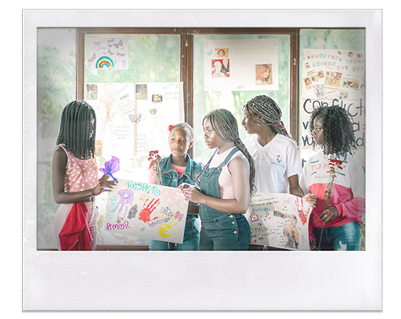Instantánea. 5 niñas y adolescentes afro sostienen flores y carteles hechos a mano. Carteles pegados en la ventana