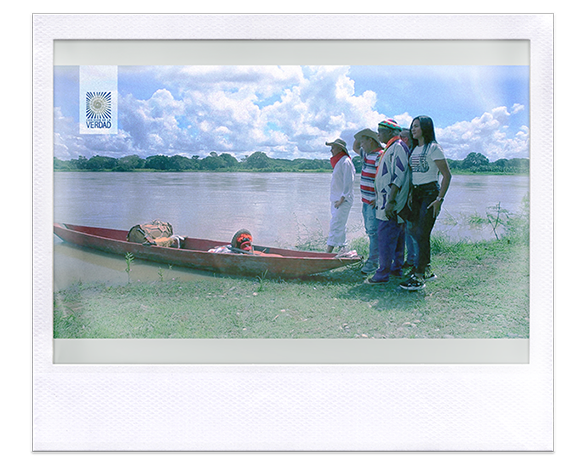 Instantánea. Personas de pie a la orilla del río, delante una canoa con una tambora