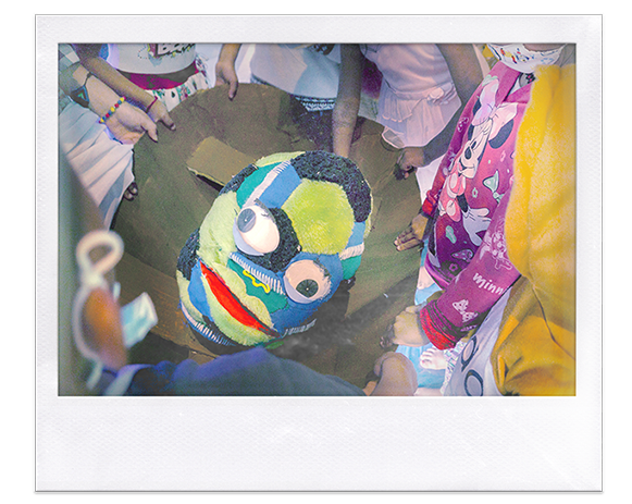 Instantánea. Grupo de niños sostienen con sus manos la base de una marioneta de ojos saltones hecha de retazos de tela multicolor