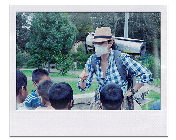 Instantánea. Grupo de niños en un parque escuchan a una mujer con morral de viaje y sombrero