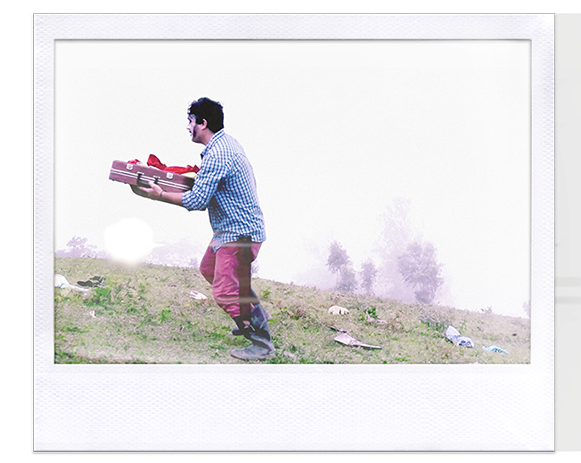 Instantánea. Hombre en el campo, con el rostro pintado, sostiene una valija cubierta con una tela roja