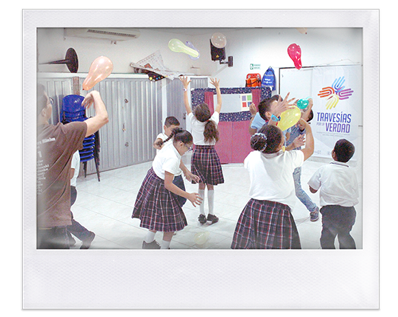 Instantánea. Niñas y niños en salon de clase y uniforme, juegan con bombas de colores