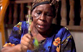 Rostro de mujer afro que sostiene en su mano una planta. De fondo se ven unas barandas de madera y una silla